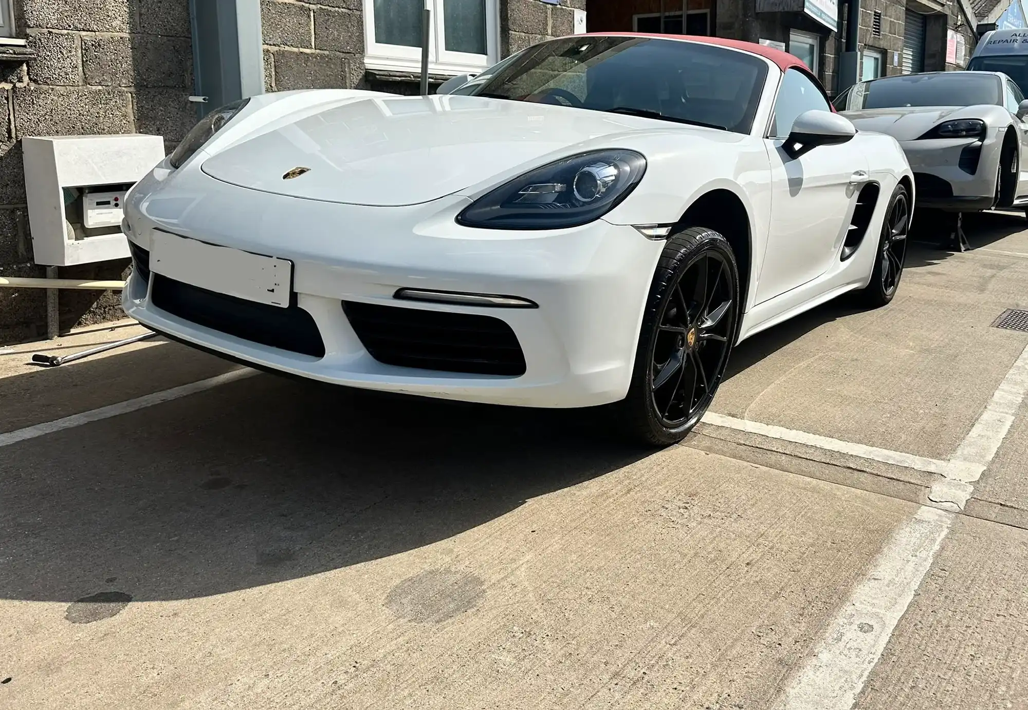 White Porsche convertible with black wheels parked on a concrete surface next to buildings.
