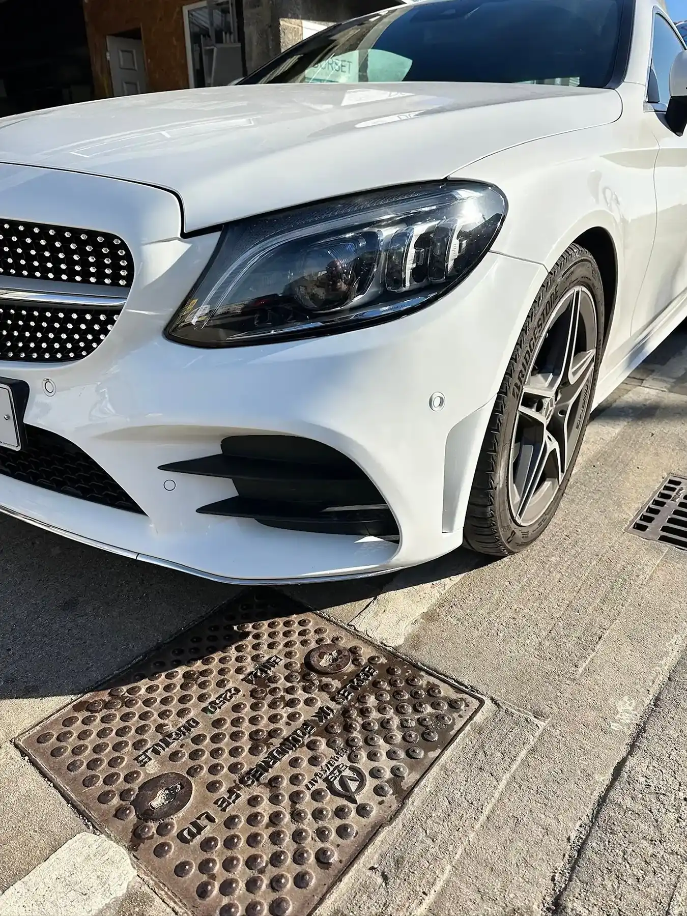 Close-up of a white luxury car front showing headlight, black grille, and alloy wheel on concrete.